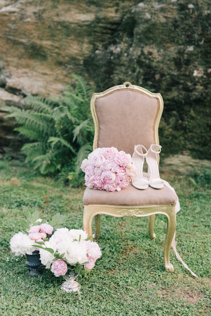 Elegant vintage chair with pink bouquet and high heels in an outdoor garden setting.